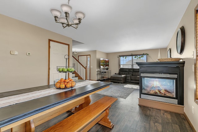 dining area featuring a multi sided fireplace, wood finished floors, a chandelier, baseboards, and stairs