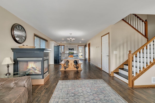 interior space with a chandelier, a multi sided fireplace, visible vents, stairs, and dark wood-style floors