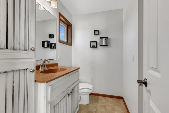 half bath with toilet, baseboards, and vanity