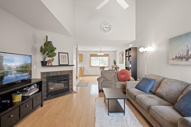 living room featuring a tiled fireplace, ceiling fan, a high ceiling, and light wood-type flooring