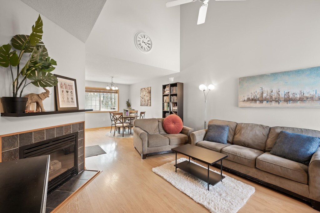 living room with hardwood / wood-style flooring, ceiling fan with notable chandelier, a tile fireplace, and a high ceiling