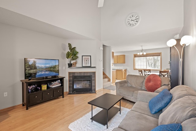 living room with a tile fireplace, a towering ceiling, a notable chandelier, and light wood-type flooring