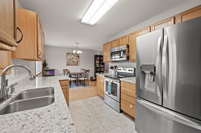 kitchen featuring hanging light fixtures, appliances with stainless steel finishes, sink, and light stone counters