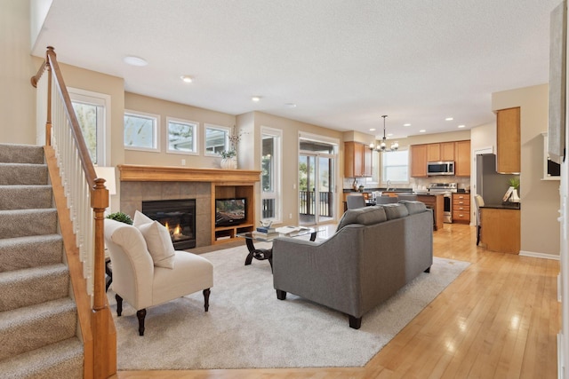 living room featuring a notable chandelier, a fireplace, a textured ceiling, and light wood-type flooring