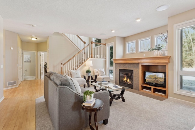 living room featuring a textured ceiling, a tile fireplace, a healthy amount of sunlight, and light wood-type flooring