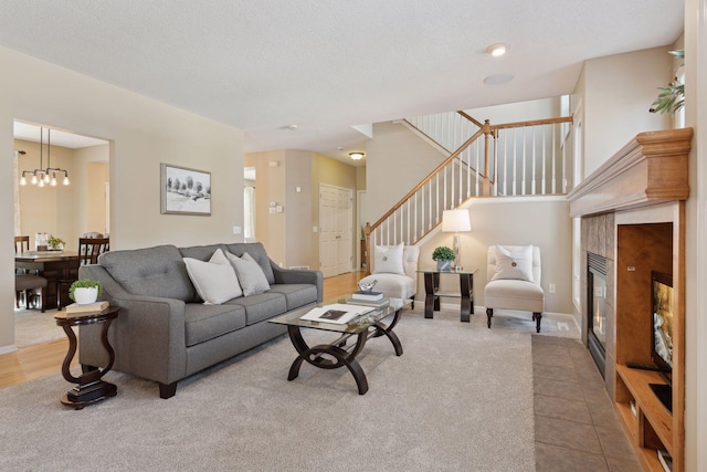 living room featuring an inviting chandelier, a tiled fireplace, and a textured ceiling