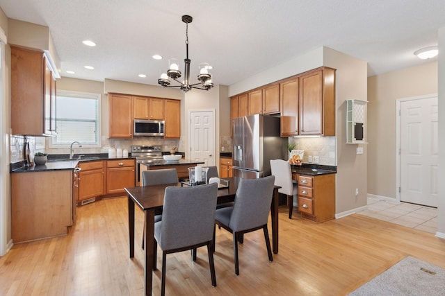 kitchen with sink, light hardwood / wood-style flooring, appliances with stainless steel finishes, tasteful backsplash, and decorative light fixtures