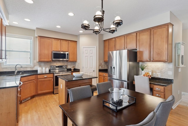 kitchen with sink, decorative light fixtures, light hardwood / wood-style flooring, a kitchen island, and stainless steel appliances