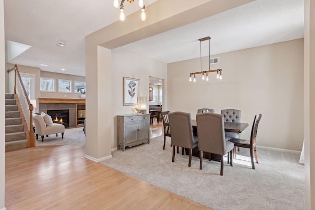 dining room with an inviting chandelier, a fireplace, and light hardwood / wood-style floors