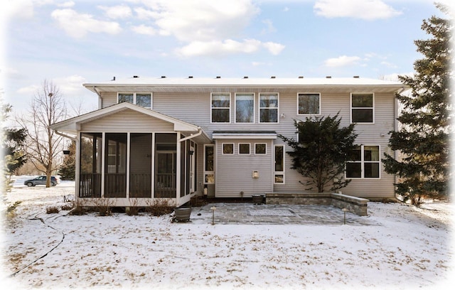 snow covered back of property with a sunroom