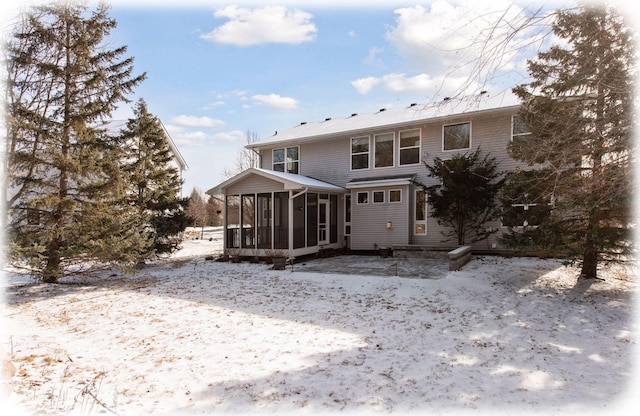 snow covered rear of property with a sunroom