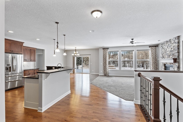 kitchen with a breakfast bar, wood-type flooring, decorative light fixtures, stainless steel fridge with ice dispenser, and a center island with sink