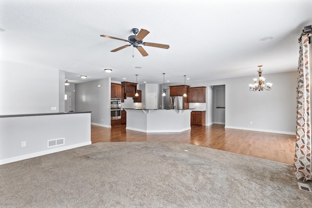 unfurnished living room with ceiling fan with notable chandelier and dark colored carpet