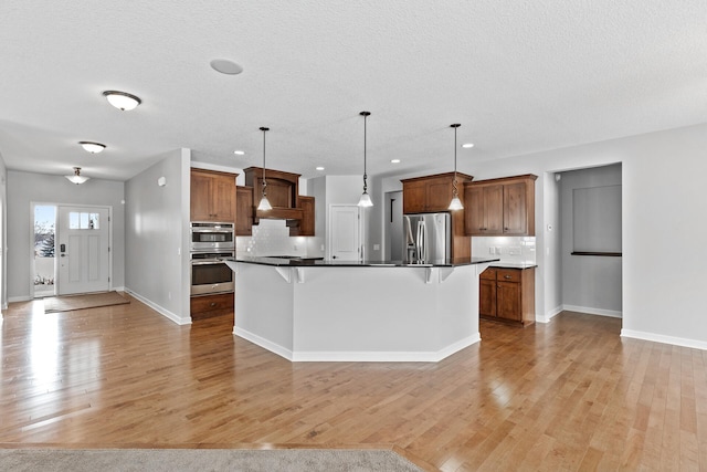 kitchen featuring appliances with stainless steel finishes, pendant lighting, tasteful backsplash, an island with sink, and a kitchen bar