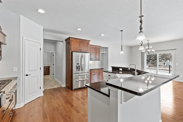 kitchen featuring a large island, sink, stainless steel fridge with ice dispenser, decorative light fixtures, and light wood-type flooring