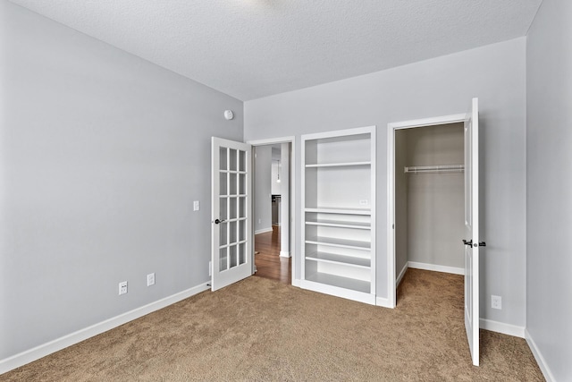 unfurnished bedroom with a spacious closet, carpet flooring, a textured ceiling, and a closet