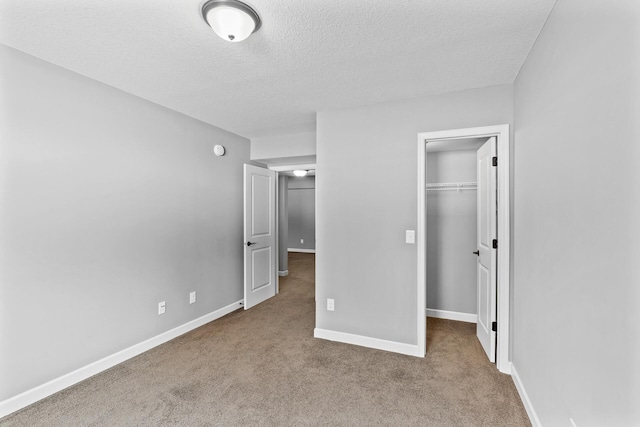 unfurnished bedroom with a walk in closet, light carpet, a textured ceiling, and a closet