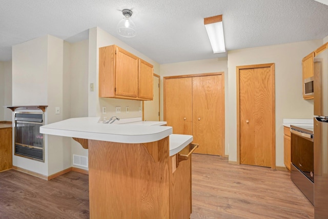 kitchen with a breakfast bar, light hardwood / wood-style floors, a textured ceiling, stainless steel electric stove, and kitchen peninsula