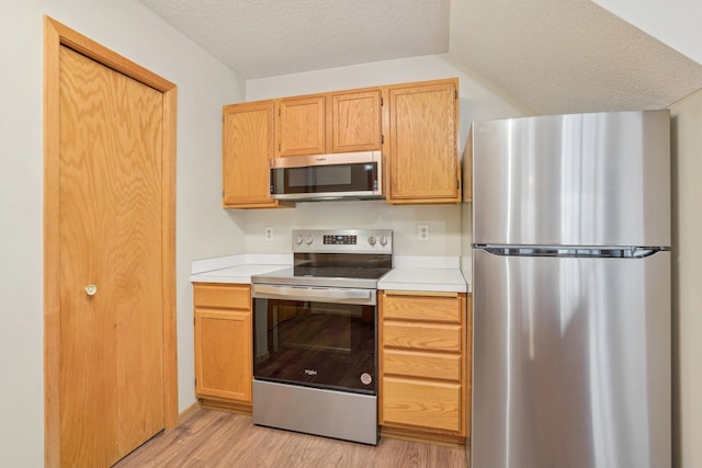 kitchen with appliances with stainless steel finishes, light brown cabinetry, a textured ceiling, and light wood-type flooring