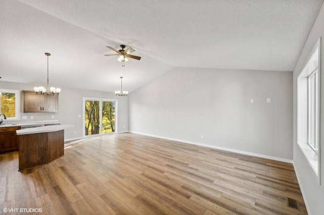 unfurnished living room with sink, ceiling fan with notable chandelier, light hardwood / wood-style flooring, and vaulted ceiling