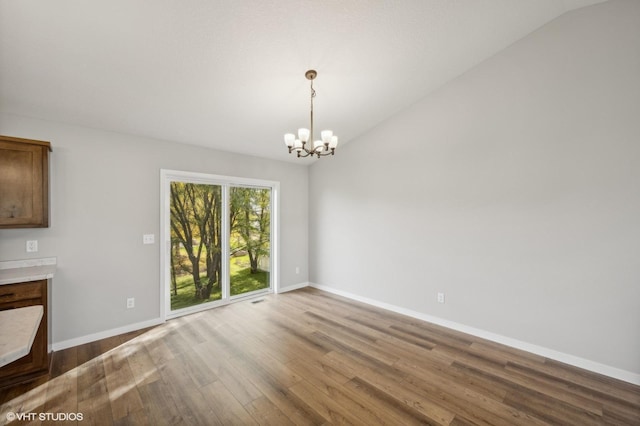 unfurnished dining area with lofted ceiling, hardwood / wood-style floors, and an inviting chandelier