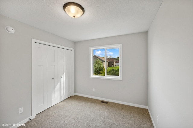 unfurnished bedroom with light colored carpet, a closet, and a textured ceiling