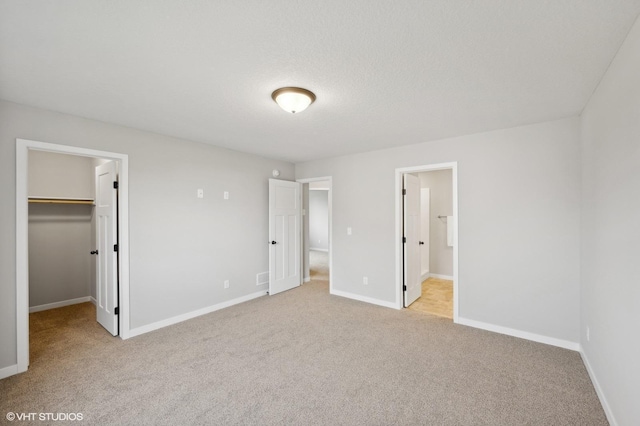 unfurnished bedroom featuring a walk in closet, light carpet, a textured ceiling, ensuite bath, and a closet