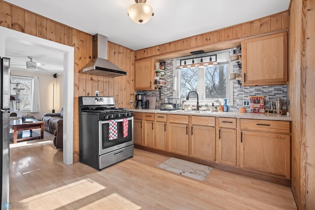 kitchen with a sink, wall chimney exhaust hood, light countertops, and gas range