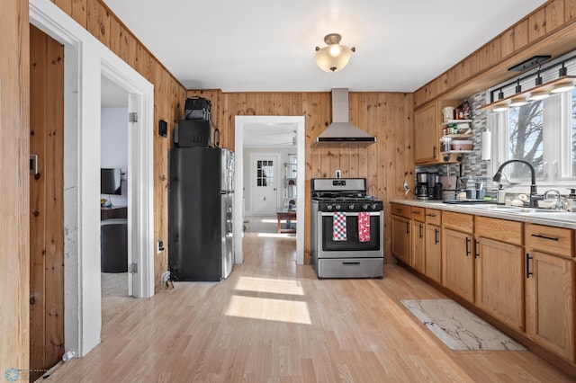 kitchen with stainless steel appliances, a sink, light countertops, light wood-type flooring, and wall chimney exhaust hood