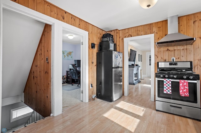 kitchen featuring stainless steel appliances, wood walls, wall chimney exhaust hood, and wood finished floors