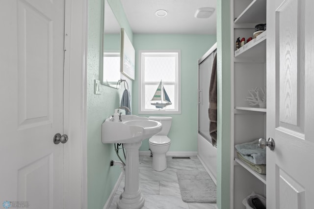 bathroom featuring marble finish floor, baseboards, toilet, and bath / shower combo with glass door