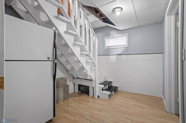 below grade area featuring concrete block wall, a paneled ceiling, stairway, freestanding refrigerator, and light wood-type flooring