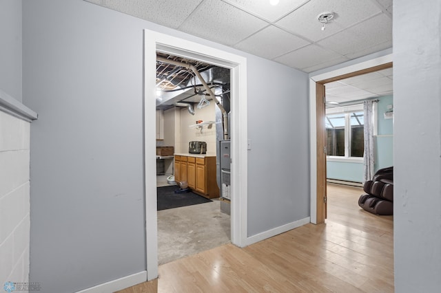 corridor with a baseboard heating unit, light wood-type flooring, a paneled ceiling, and baseboards