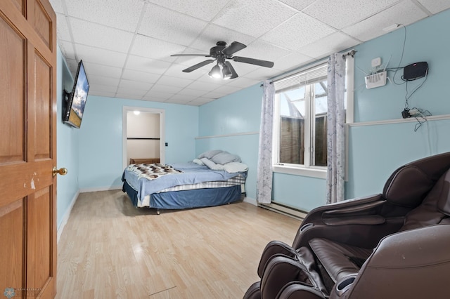 bedroom with baseboards, light wood-style flooring, ceiling fan, a baseboard radiator, and a paneled ceiling