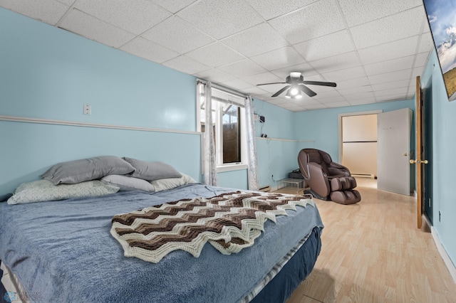 bedroom featuring light wood-style floors, a drop ceiling, baseboard heating, and a ceiling fan