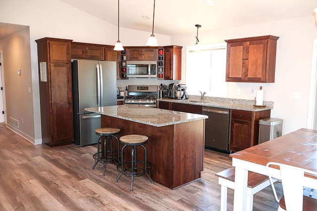 kitchen featuring vaulted ceiling, a kitchen island, appliances with stainless steel finishes, decorative light fixtures, and light stone counters