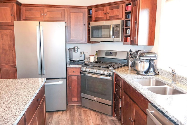 kitchen with appliances with stainless steel finishes, sink, light stone counters, and light hardwood / wood-style flooring