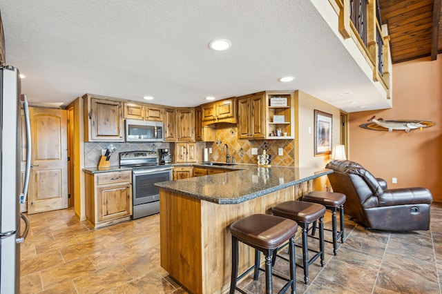 kitchen featuring a peninsula, a sink, stainless steel appliances, a kitchen breakfast bar, and tasteful backsplash