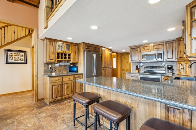 kitchen featuring a sink, appliances with stainless steel finishes, a peninsula, decorative backsplash, and baseboards