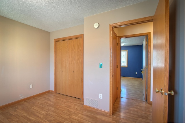 unfurnished bedroom featuring a textured ceiling, light wood-type flooring, and a closet