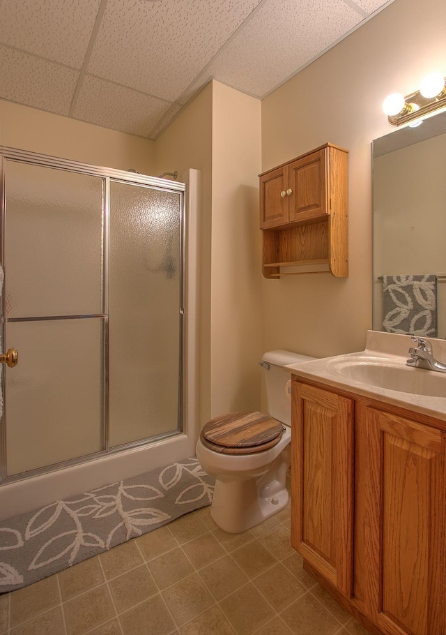 bathroom featuring toilet, a shower with shower door, vanity, tile patterned flooring, and a drop ceiling