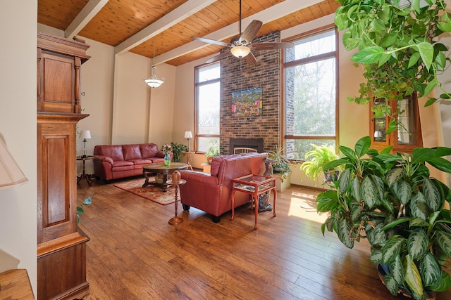 living room with wood ceiling, ceiling fan, dark hardwood / wood-style floors, a brick fireplace, and beamed ceiling