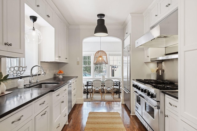 kitchen featuring high end appliances, sink, white cabinetry, and decorative light fixtures