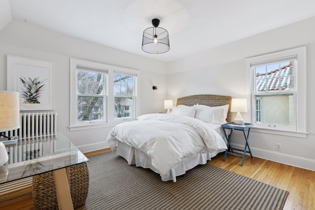 bedroom with multiple windows, hardwood / wood-style flooring, and radiator heating unit