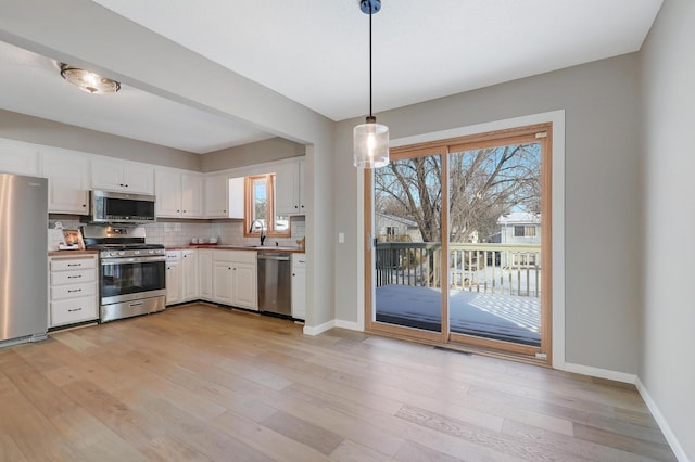 kitchen with white cabinetry, appliances with stainless steel finishes, hanging light fixtures, and light wood-type flooring