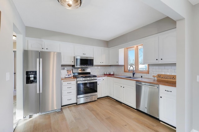 kitchen featuring sink, butcher block countertops, white cabinetry, light hardwood / wood-style flooring, and appliances with stainless steel finishes