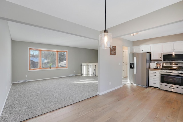 kitchen featuring white cabinetry, stainless steel appliances, hanging light fixtures, and light wood-type flooring