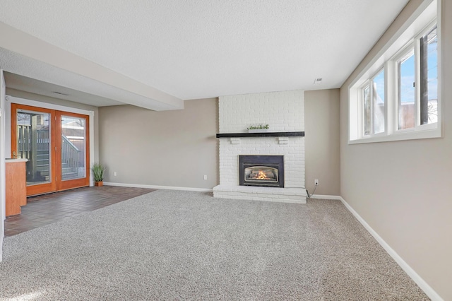 unfurnished living room with dark carpet, a fireplace, french doors, and a textured ceiling