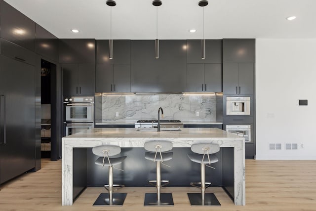 kitchen featuring light stone counters, decorative light fixtures, a breakfast bar area, and an island with sink