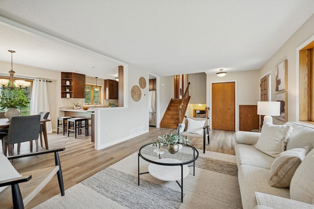 living area with baseboards, a notable chandelier, stairway, and light wood-type flooring